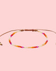 A multi colored beaded bracelet on a pink background with an adjustable tie.