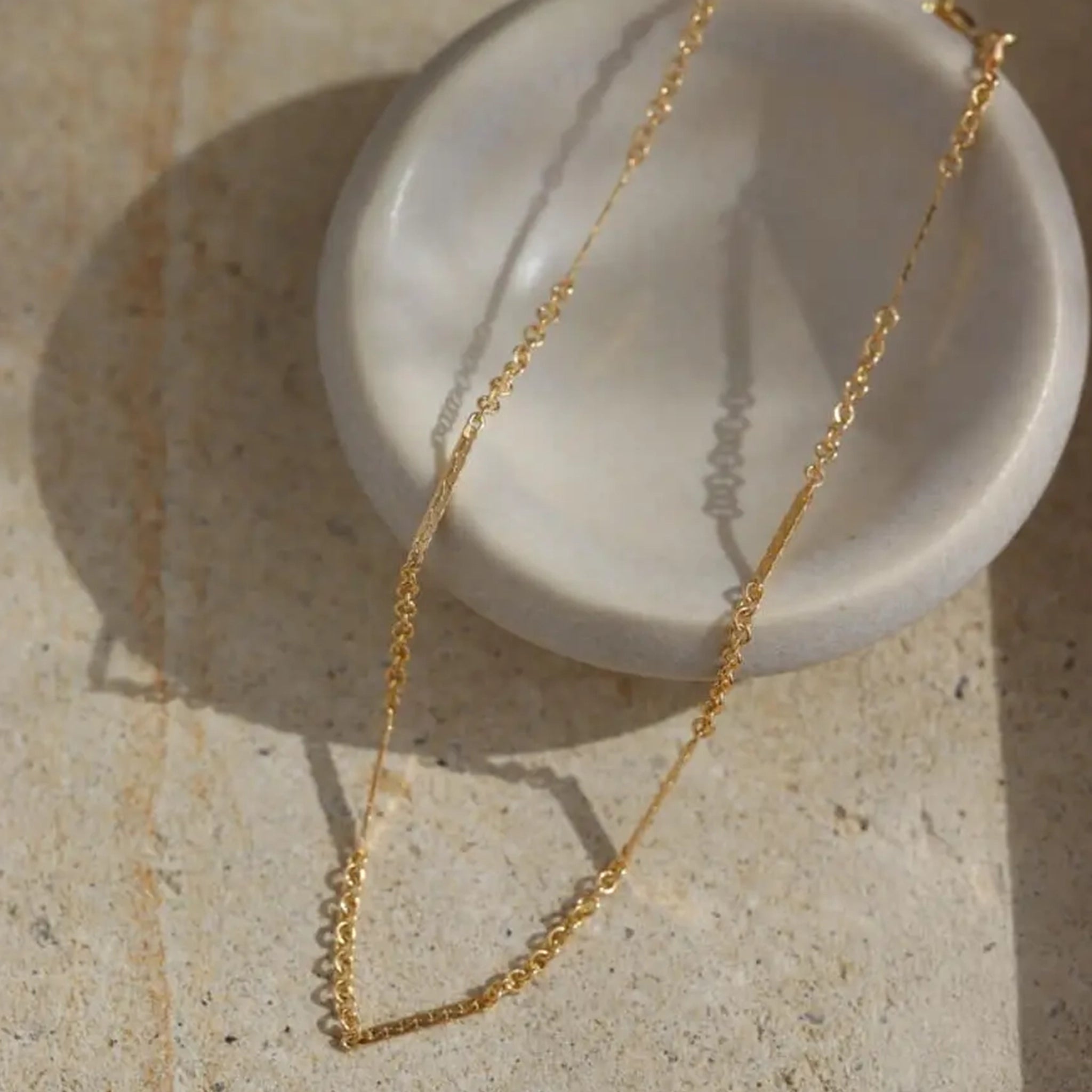 A gold chain bracelet draped over a stone jewelry holder. 