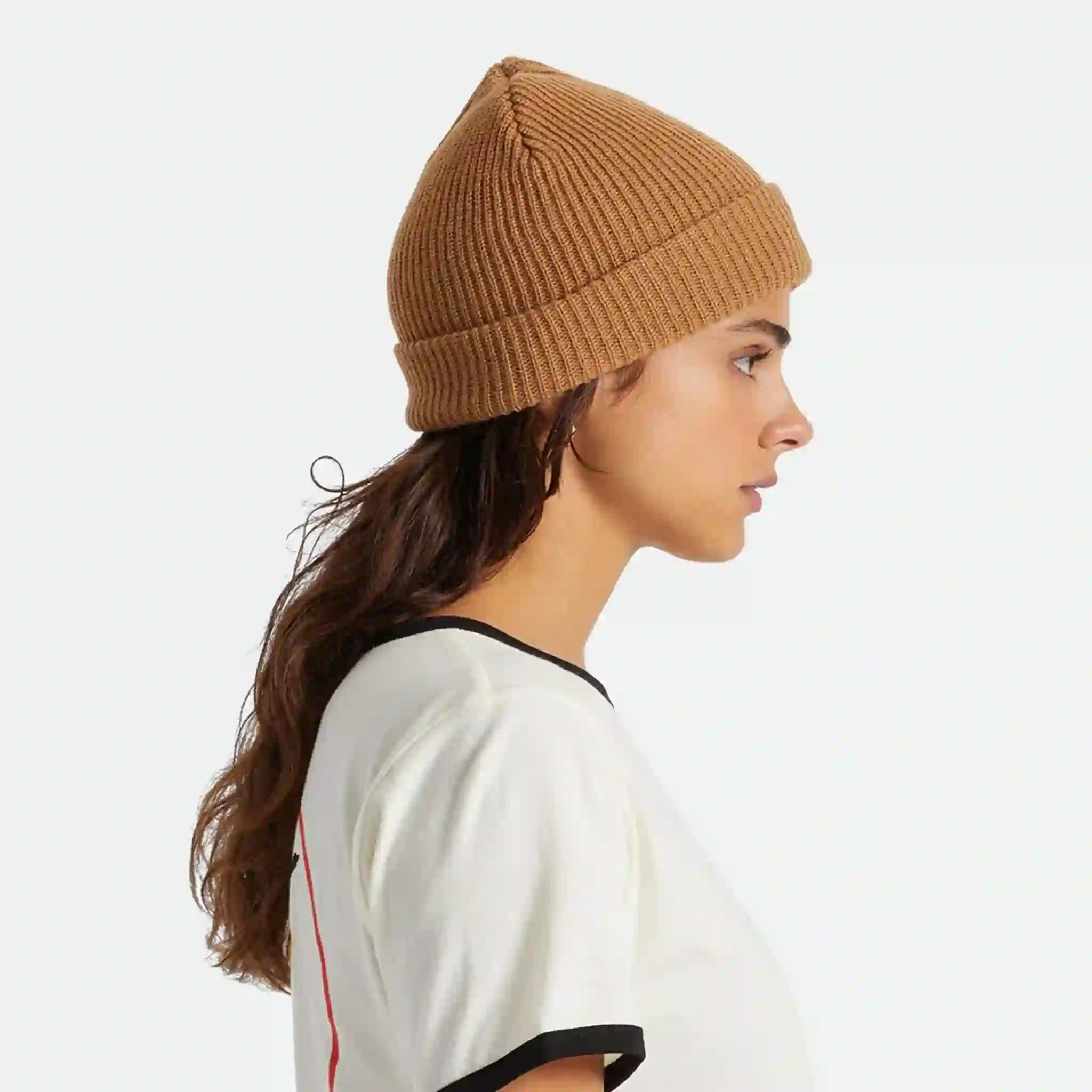 On a white background is a model wearing a tan ribbed beanie. 
