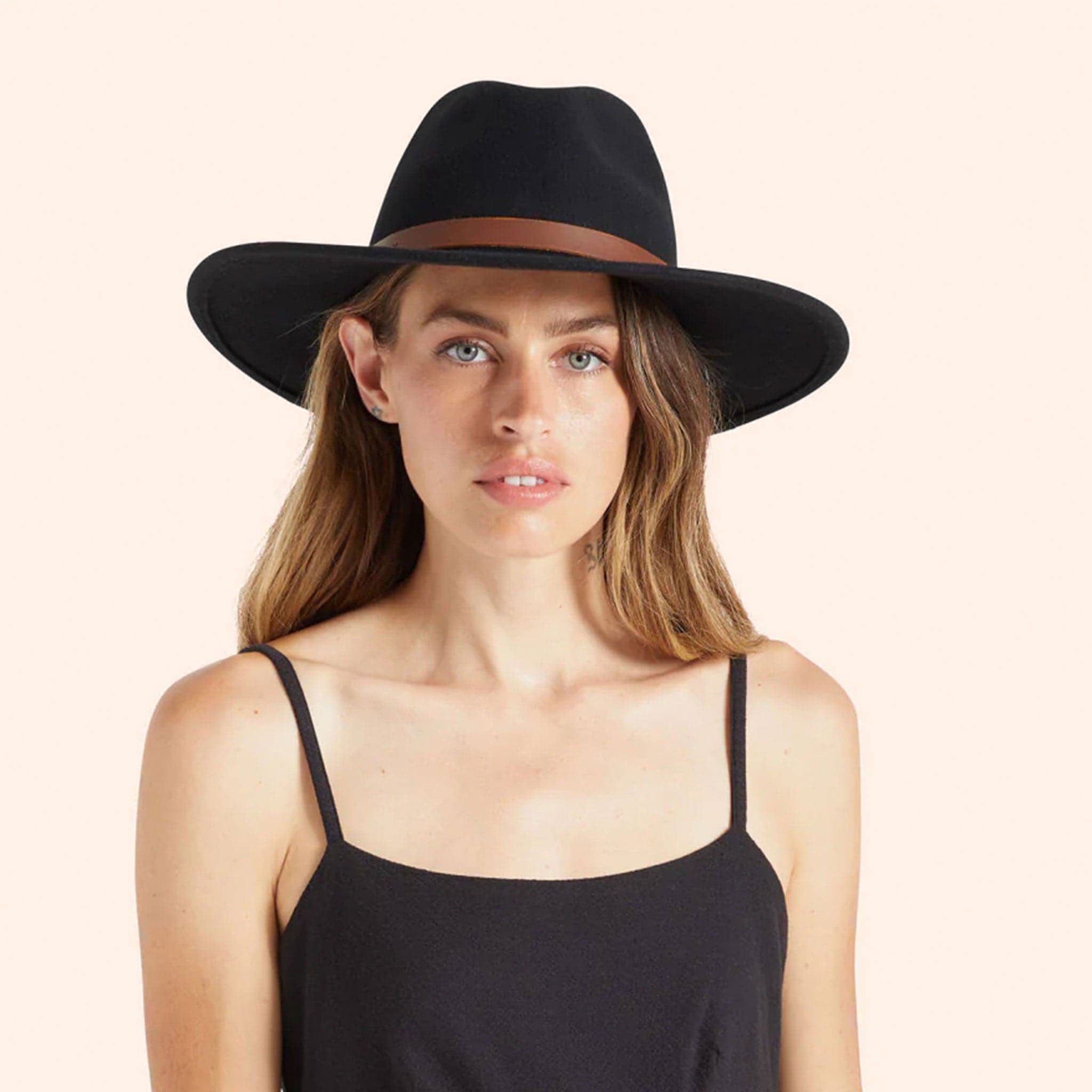 model wearing a black hat with a stiff brim and a brown leather strap around the base.
