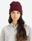 On a white background is a model wearing a mahogany colored knit beanie.