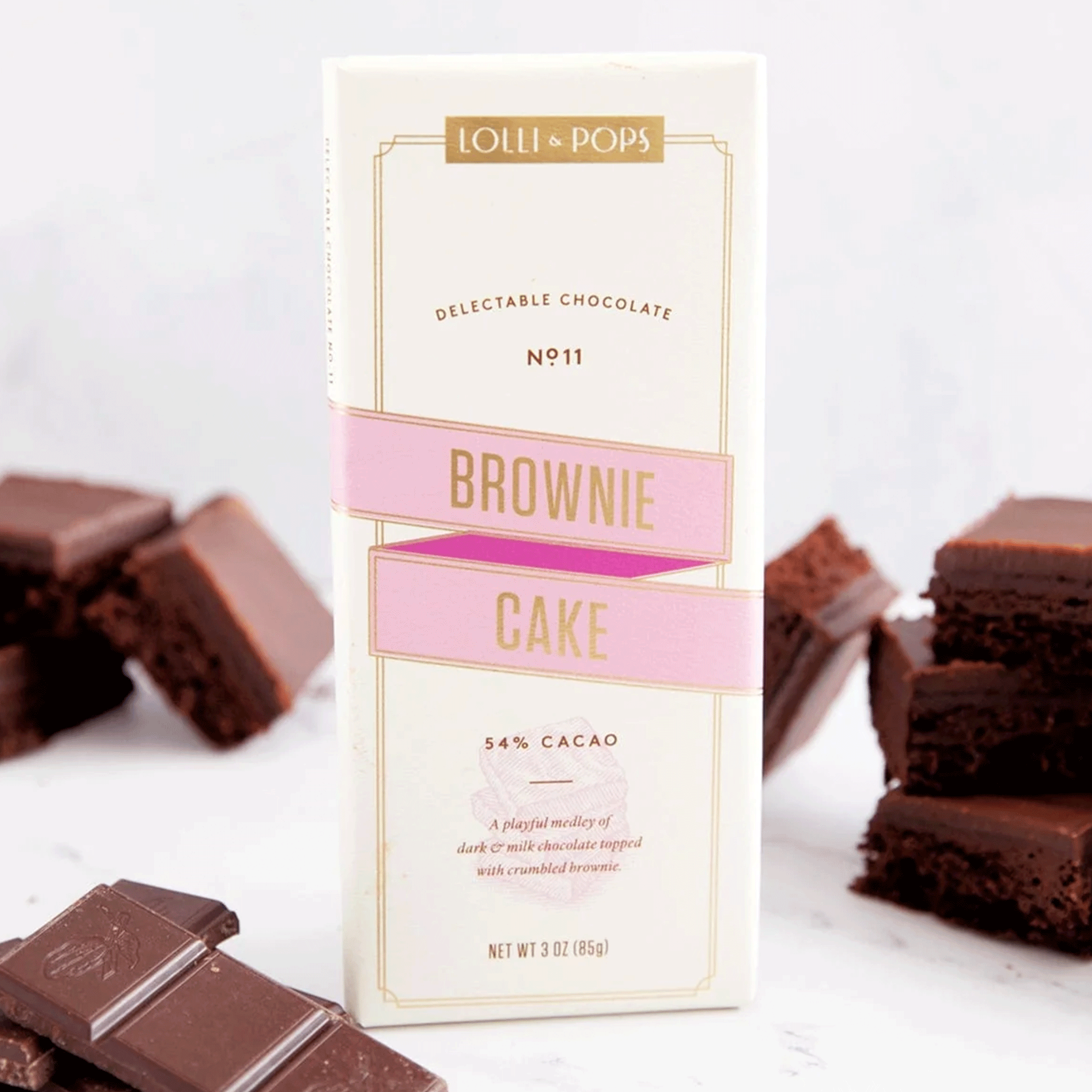 On a white background surrounded by chocolate and brownies is a neutral package filled with a chocolate bar and text on the front that reads, "Lolli & Pops Brownie Cake". 