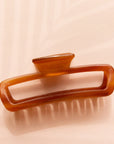On a light pink background is an amber colored rectangle claw clip with slightly rounded edges.