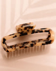 On a light pink background is a light beige tortoise print rectangle claw clip with rounded edges.