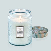 A blue glass candle sits in the middle of image. The label on the candle reads, "Voluspa California Summers"