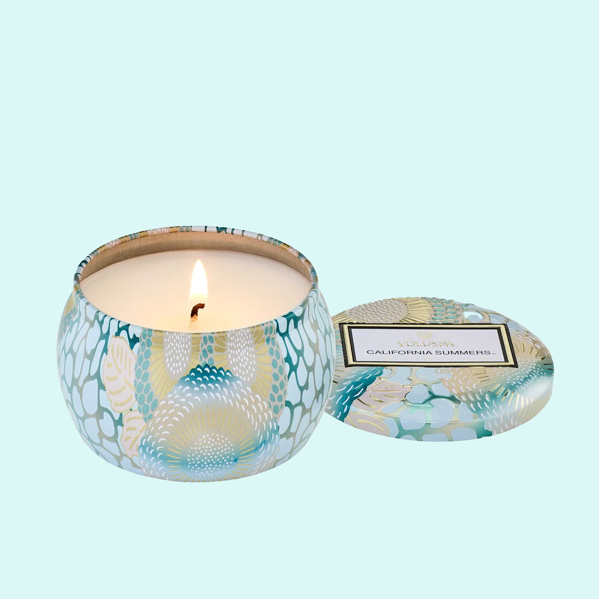 On a blue background is a light blue decorative mini tin candle with a lid and a rectangle label that reads, "Voluspa California Summers". 