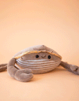 On a tan background is a grey ish brown crab stuffed toy with a sweet smiling face.