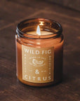 On a brown background is an amber colored jar candle with a yellow label and white text that reads, "Wild Fig & Citrus".