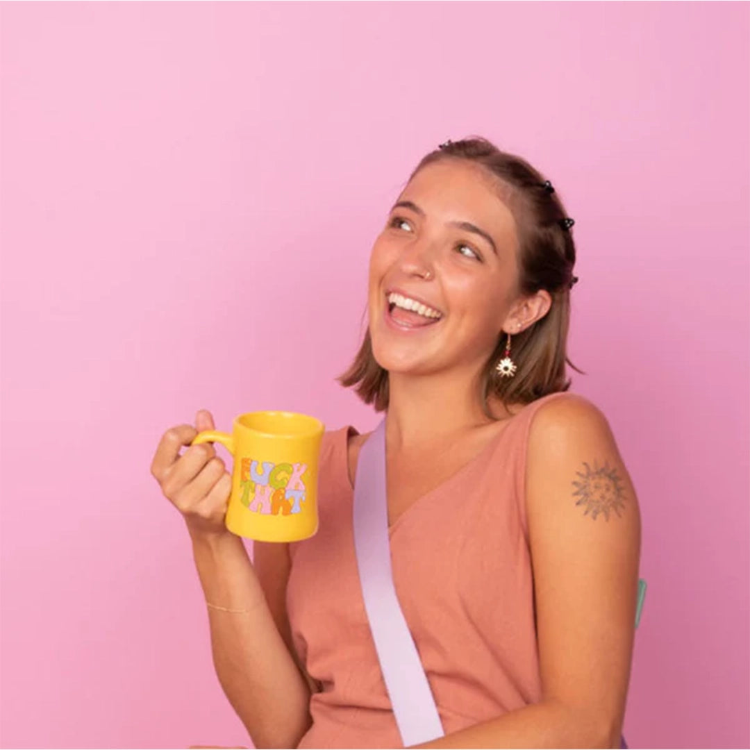 On a pink background is a yellow diner style mug that reads, "Fuck That" in multi colored text.
