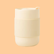 On a peachy background is a butter yellow ceramic tumbler with a silicone sleeve.