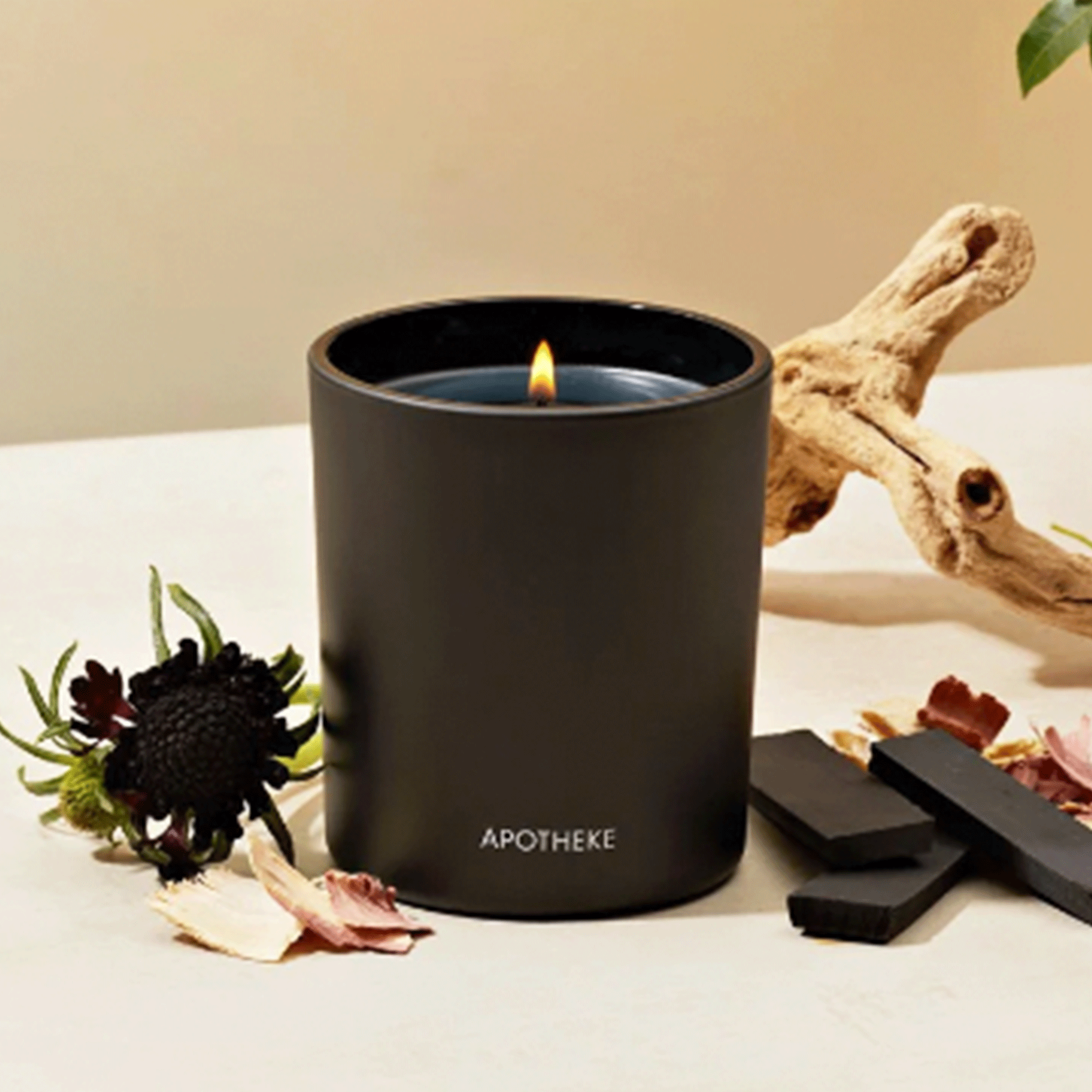 On a tan background is a black jarred candle with white text at the bottom that reads, &quot;Apotheke&quot;. 