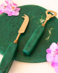 A brass bottle opener with a dark green resin handle.