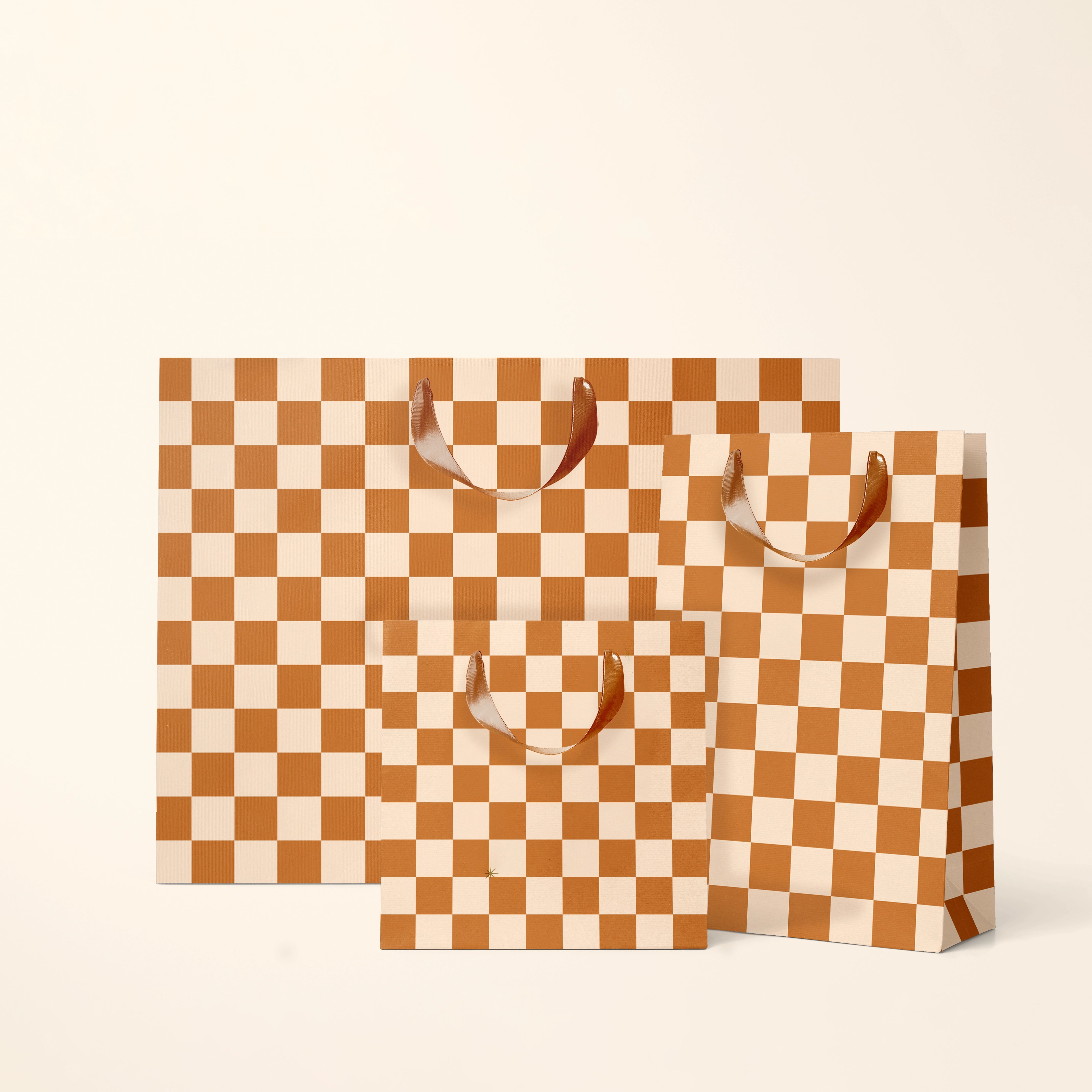 On a cream background is three different sized burnt orange and ivory checkered gift bags. 