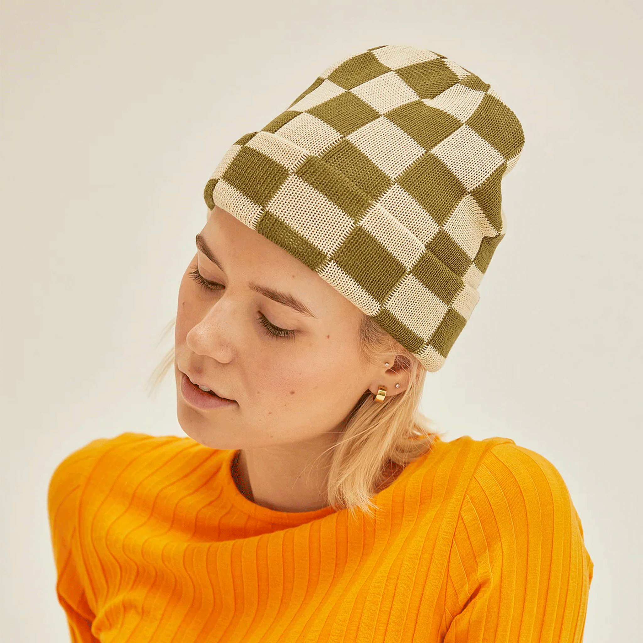 A model wearing a green and ivory checker pattern knit beanie. 