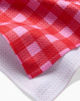 A red and pink gingham print tea towel with a waffle weave.