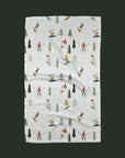 On a green background is a white waffle knit kitchen towel with a ski and snowboard pattern.