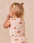 A light pink / peach colored jumpsuit with short sleeves and a cherry print.