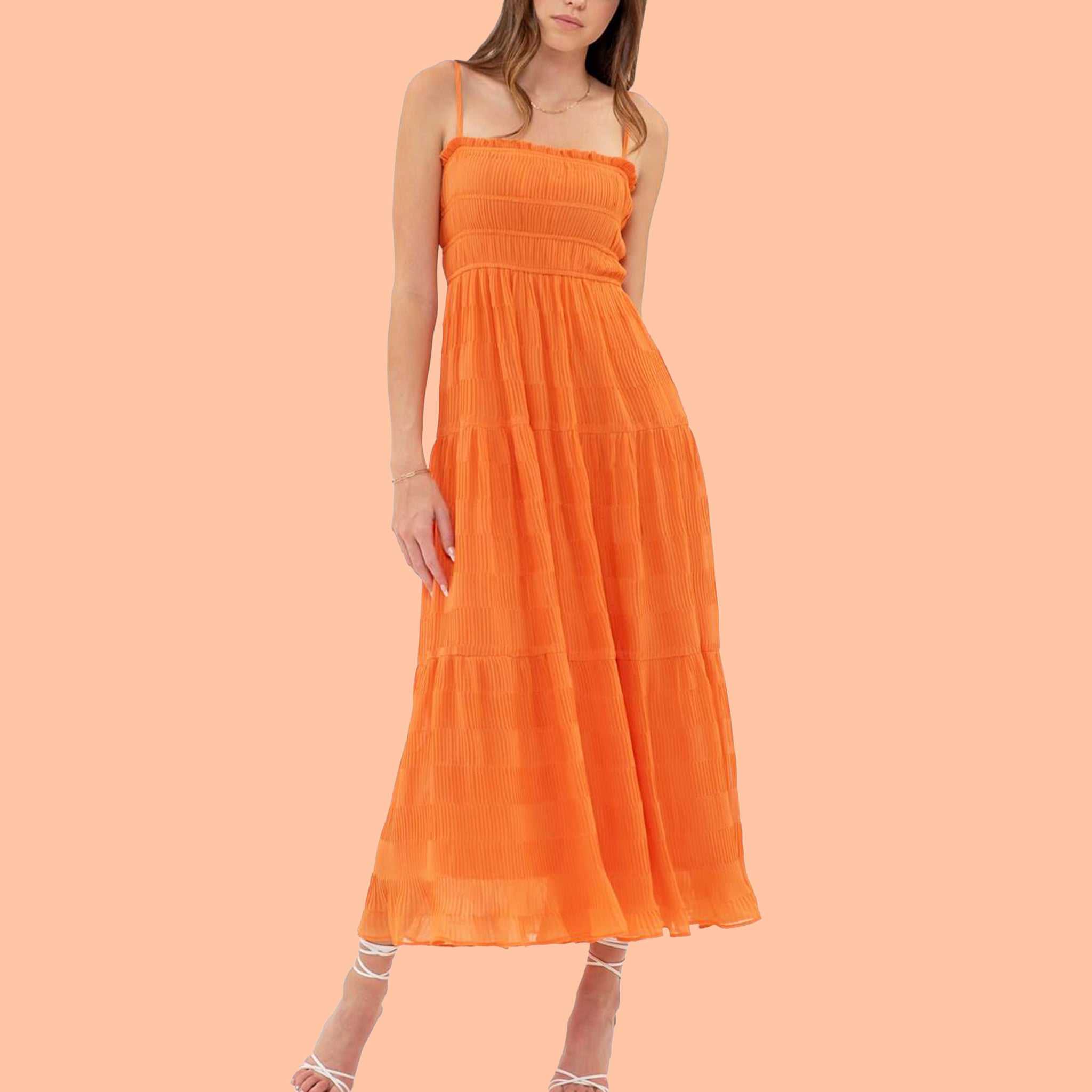 On a peach background is vibrant orange tiered midi dress with a smocked bodice and spaghetti straps. 