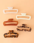 On a peachy background is a variety of rectangle claw clips in tortoise shades, an amber color and two different whites.