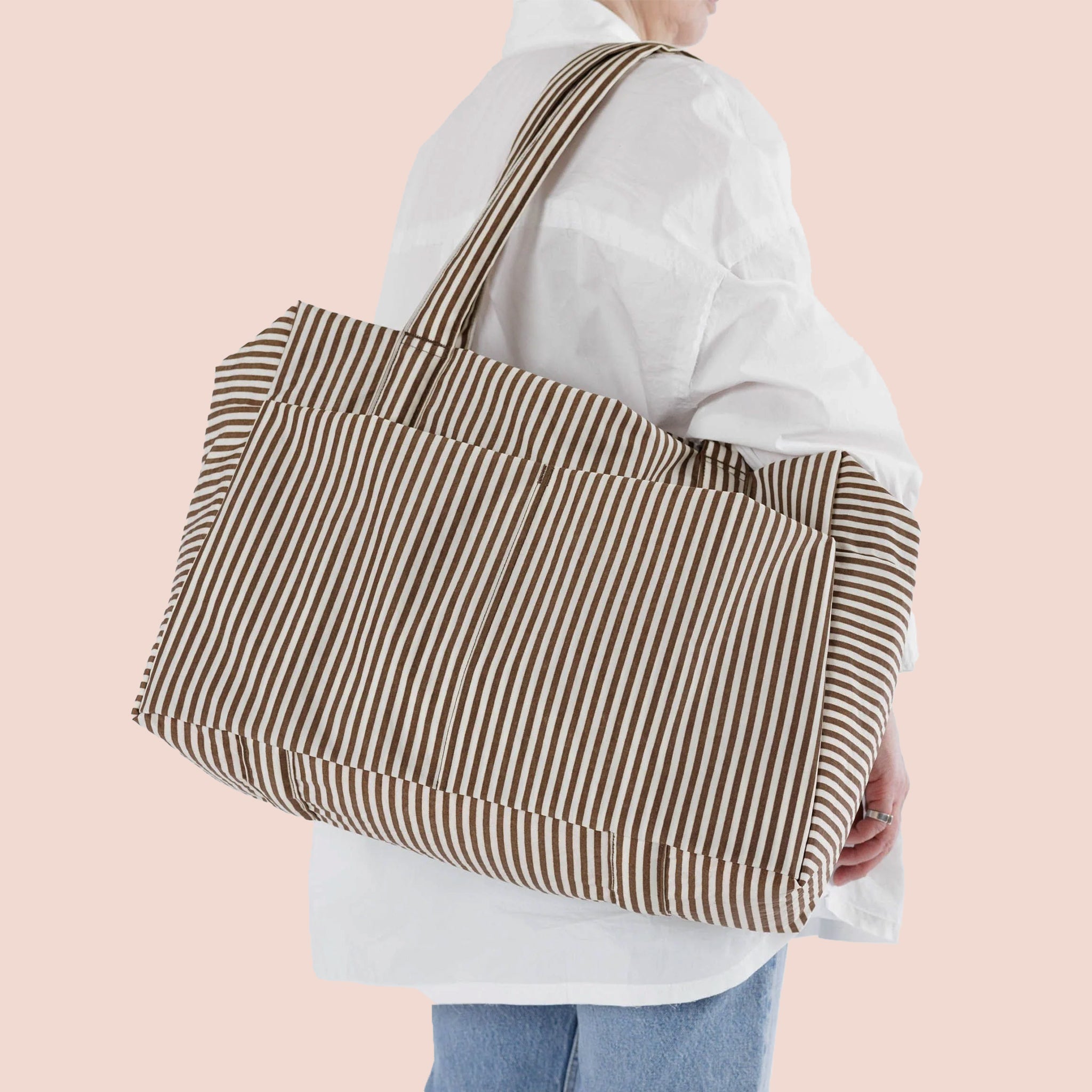 On a light pink background is a brown  and white striped travel bag tote. 