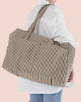 On a light pink background is a brown and white striped travel bag tote.
