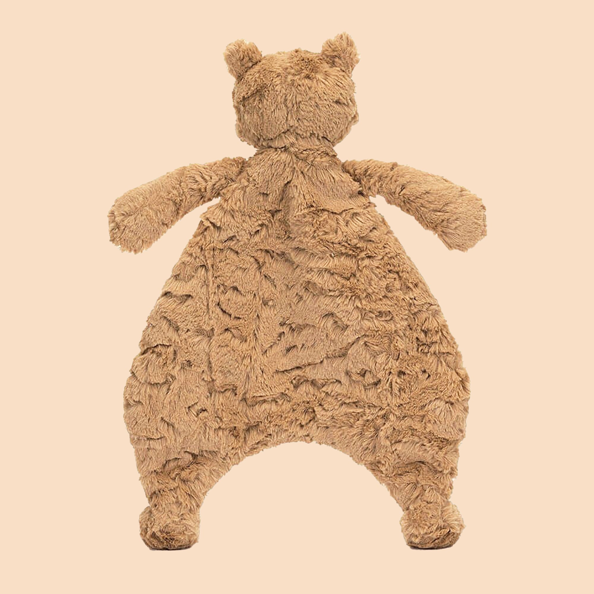 On a tan background is a stuffed toy bear head attached to a furry blanket shaped like a the bear's shape.