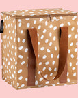 On a pink background is a brown cooler bag with white spots and a darker brown strap.