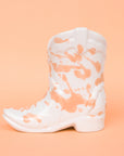 On a peachy background is a white and peach speckled cowboy boot shaped candle.