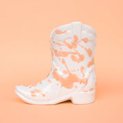 On a peachy background is a white and peach speckled cowboy boot shaped candle.