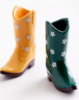 On a white background is a pair of cowboy boot shaped salt and pepper shakers. One is a yellow color with a white floral pattern and the other green with a white floral print.