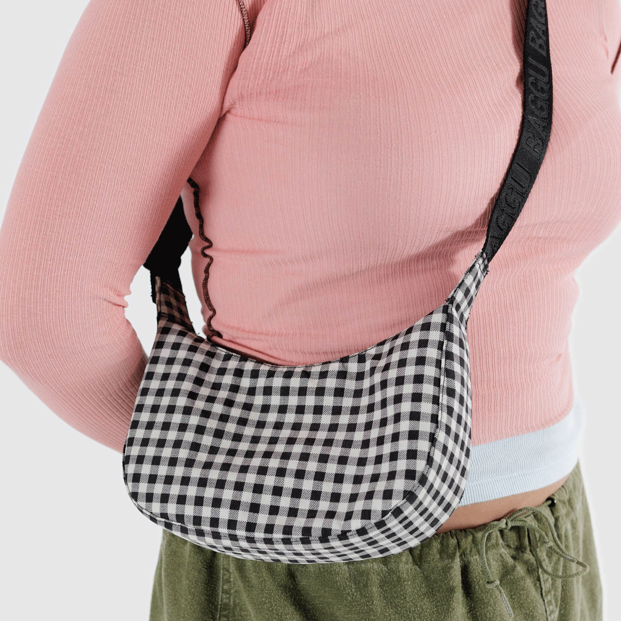 A black and white gingham printed crescent shaped nylon handbag with a black adjustable strap that can go from a shoulder bag to crossbody.
