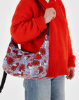 A blue and red floral and Snoopy print crescent shaped nylon handbag with a black adjustable logo strap.