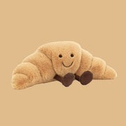 Plush toy shaped like a croissant with a smiling face on a beige background