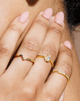 A mode wearing a gold ring with a marquise shaped cubic zirconia with three smaller stones, two towards the bottom and on the top.