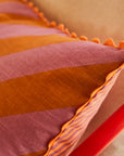 A pink and orange striped pillow with a smaller stripe on the other side and a scalloped edge.