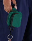 A cypress green colored fanny pack bag charm with black zippers and details.
