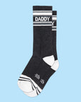A pair of black and white crew socks that are ribbed with text across the top that reads, "Daddy".