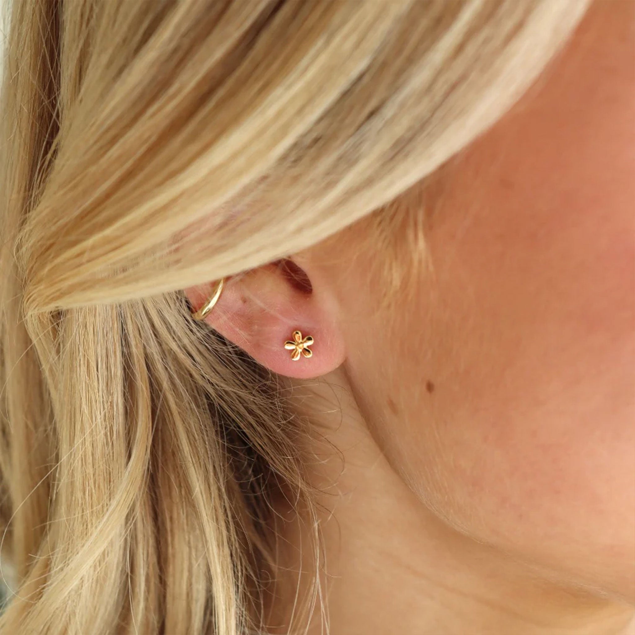 A model wearing tiny gold flower shape stud earrings. 