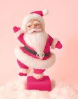 On a peach background is a hot pink flocked Santa shaped figurine holding a dancing pose.