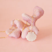 A gold chain necklace with a white shell shaped pendant.
