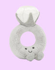 A grey stuffed toy in the shape of a diamond ring with a grey band and a white diamond shape along with a smiling face and feet on the front.