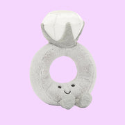 A grey stuffed toy in the shape of a diamond ring with a grey band and a white diamond shape along with a smiling face and feet on the front.