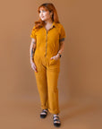 A dijon yellow utility suit with short sleeves, front pockets and a front zipper.