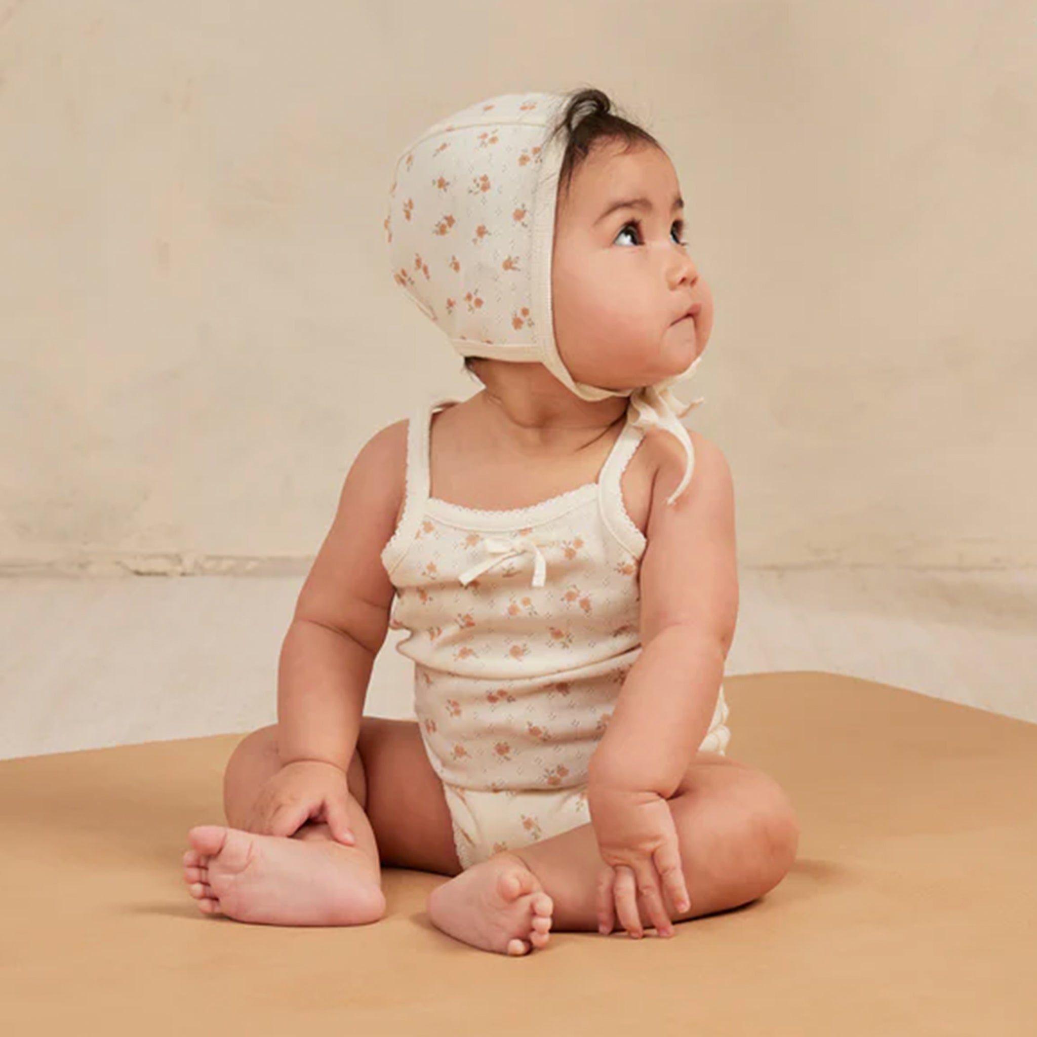 On a tan background is an ivory tank top onesie with a light orange floral print. 