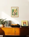 An art print of Dolly Parton signing and holding her banjo with a green background and her in pink. Frame not included.
