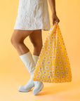 On a yellow background is a yellow, orange and white daisy pattern nylon bag.