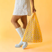 On a yellow background is a yellow, orange and white daisy pattern nylon bag.