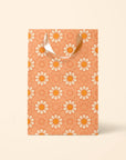 On an ivory background is the medium gift bag with an orange color and an ivory and orange daisy pattern.