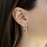 A pair of silver elongated hoop earrings.