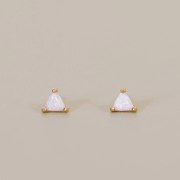 On a tan background is a triangle shaped stud earring with gold plating and a white opal stone center.